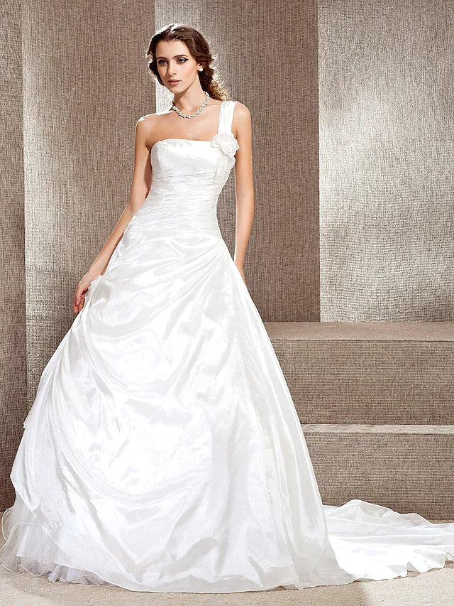 Model wearing a white one-shoulder A-line wedding dress with a long cathedral train.