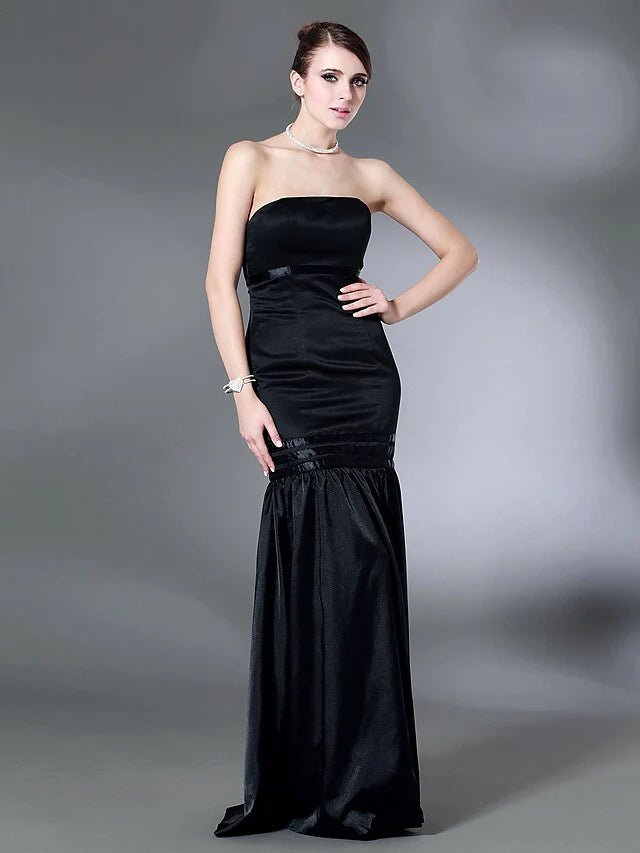 Woman wearing a dark strapless open-back floor-length dress with elegant draping, front view.