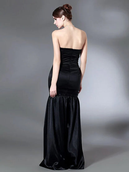 Woman in a dark strapless open-back floor-length dress with draping, side profile.