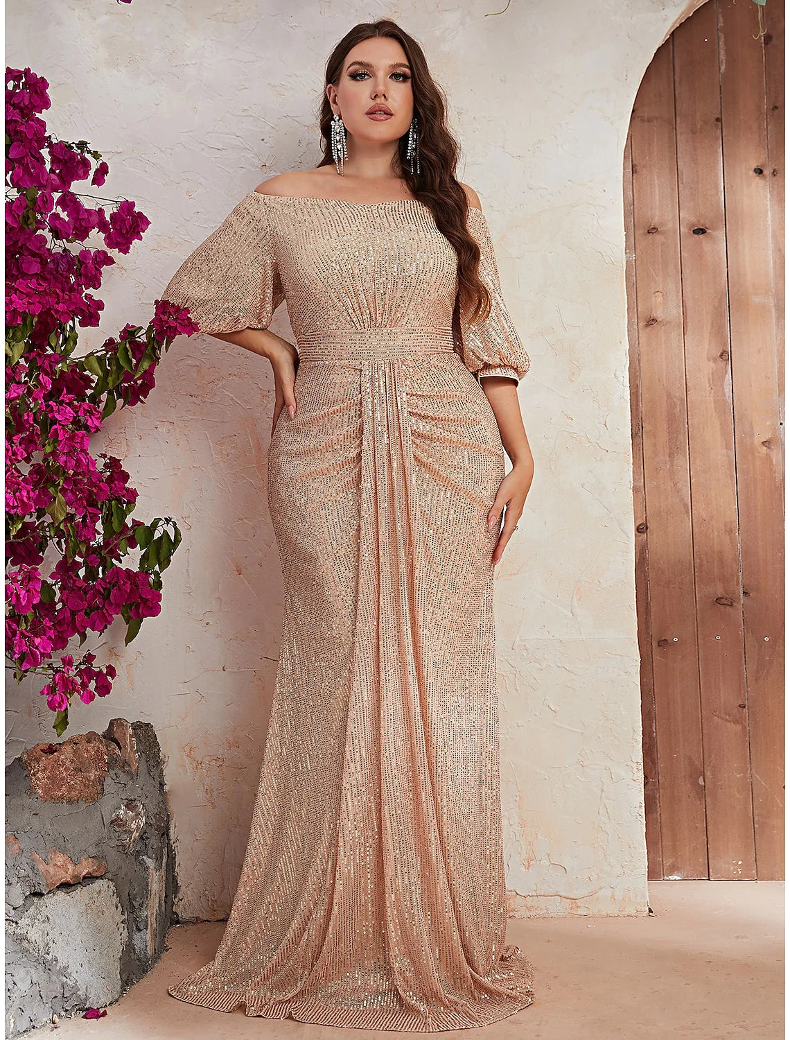 Woman wearing a sparkling A-line off-shoulder wedding guest dress with beading and a sweep train, front view.