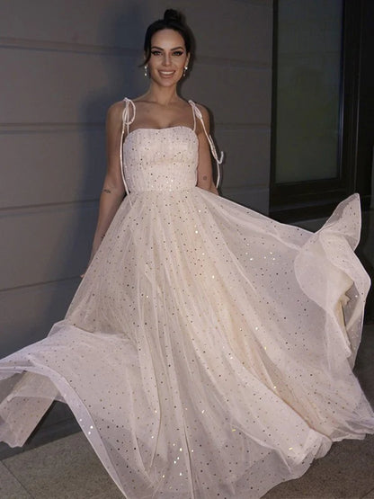 Woman wearing a sparkling A-line paillette prom dress with spaghetti straps.
